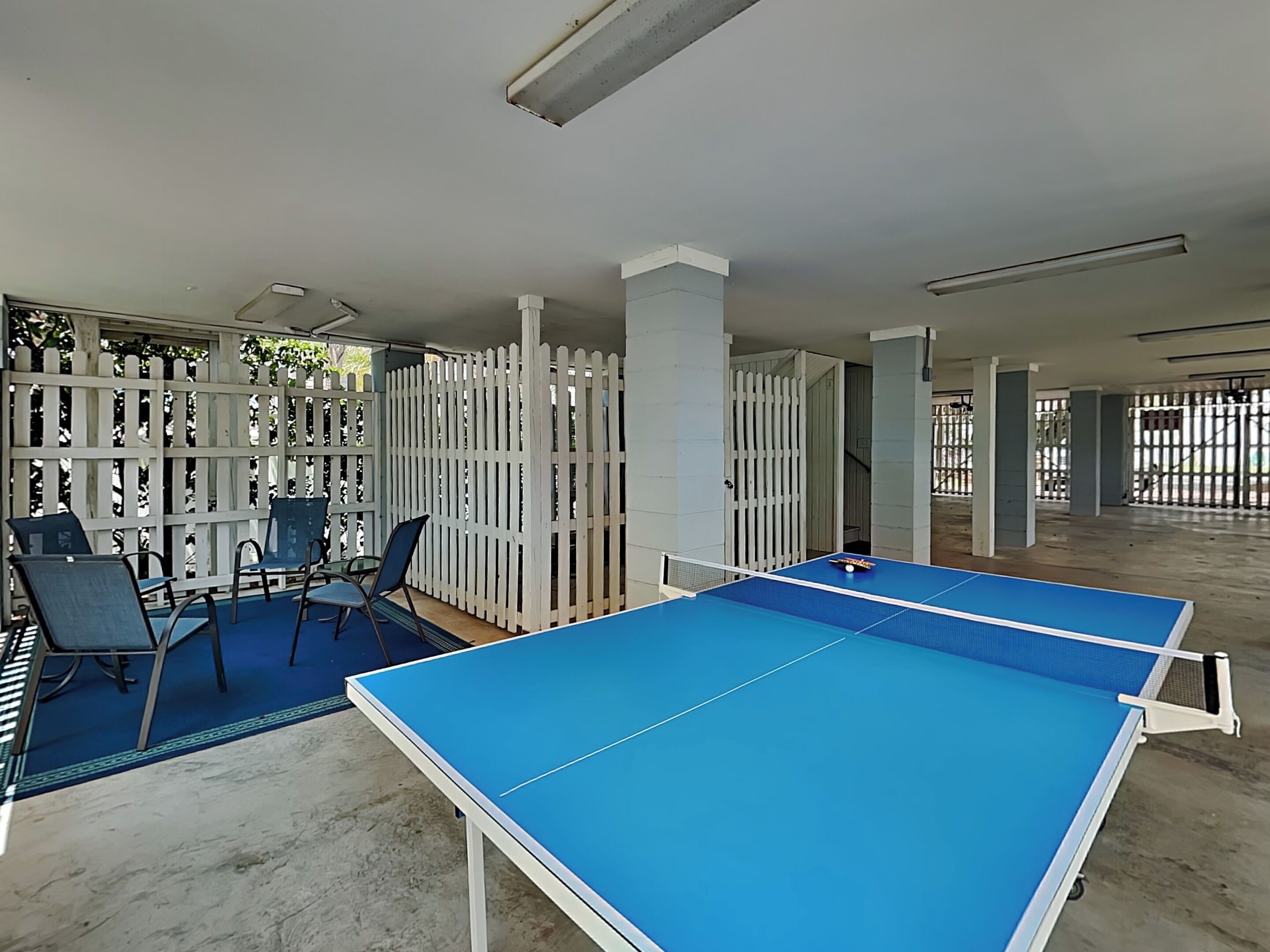 A room with a ping pong table, chairs, and a white fence.