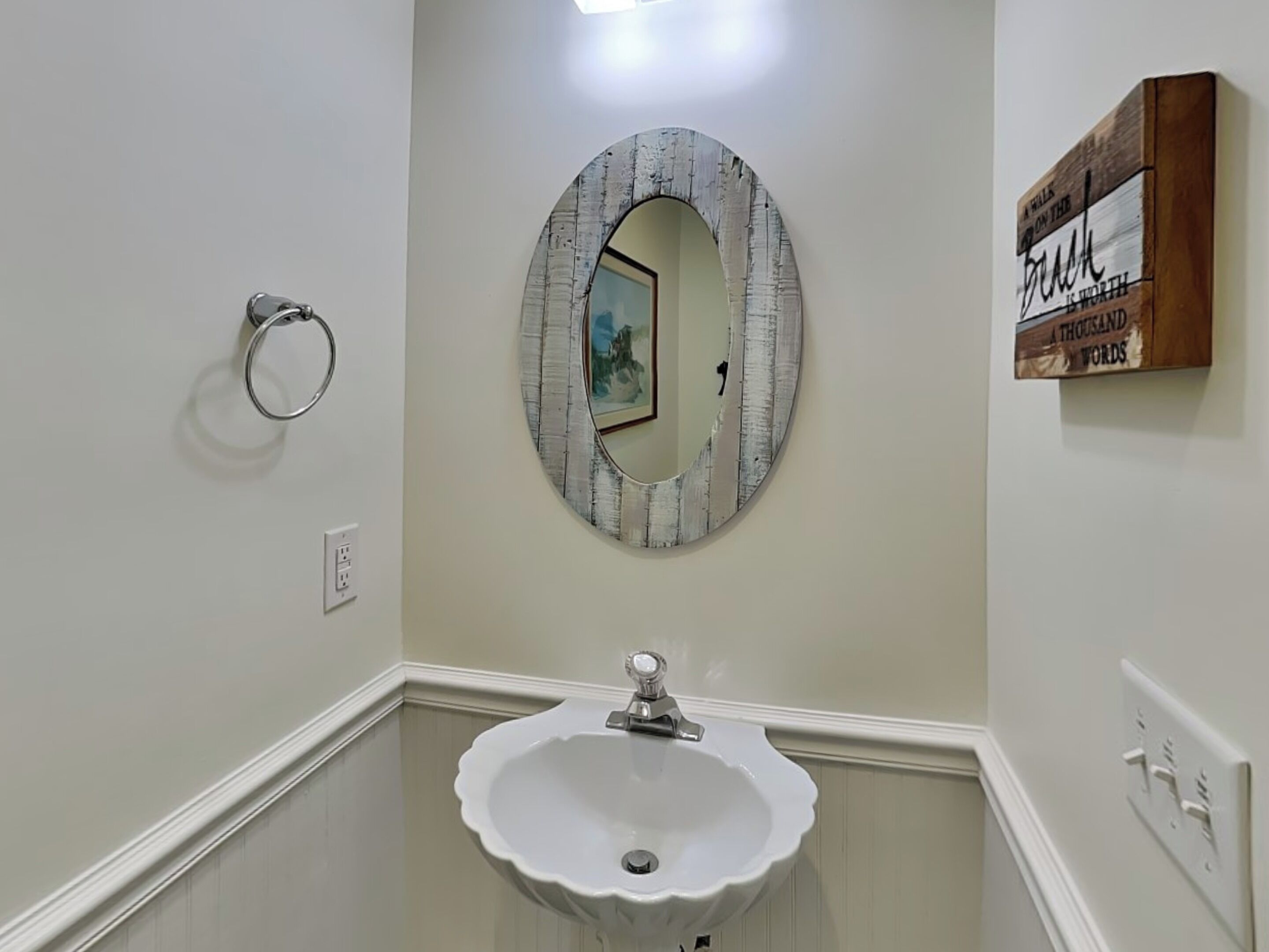 A bathroom with a round mirror, a white sink, and a wooden sign on the wall.