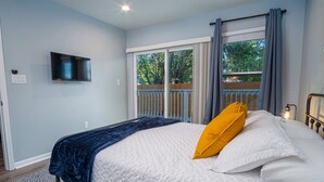 A bedroom with a bed, a TV mounted on the wall, and a view of the outdoors through a sliding door. - Escape to 4br/3ba Brand New Downtown Home (San Antonio)