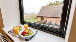 A breakfast setup on a window ledge with a view of a brick building and a grassy field. - Fawn Cottage Disabled Adapted 3 Bedroom hot tub (Alcester)