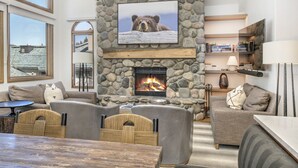 A cozy living room with a stone fireplace, comfortable seating, and a television mounted on the wall.
