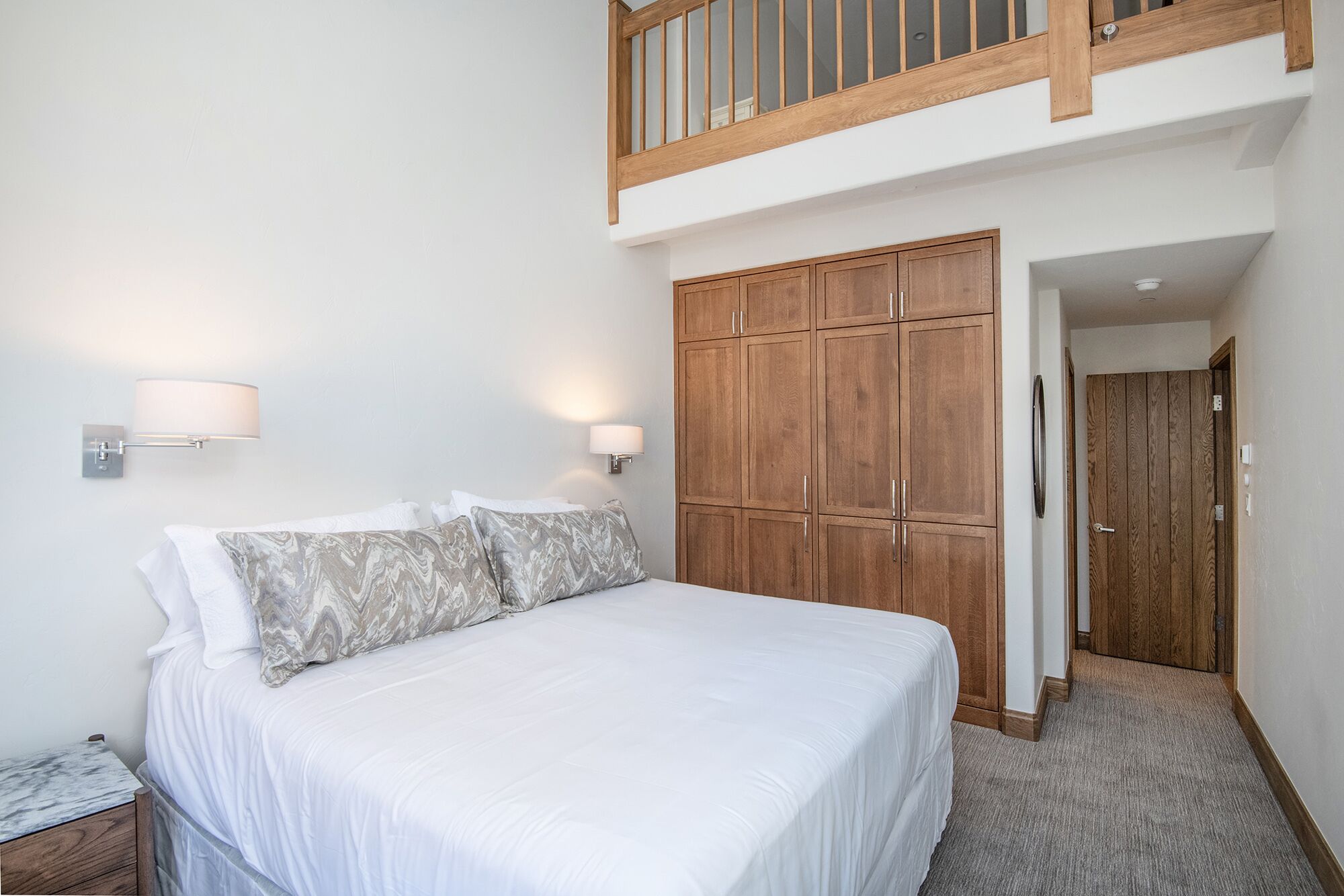 A bedroom with a large bed, wooden wardrobe, and a balcony.
