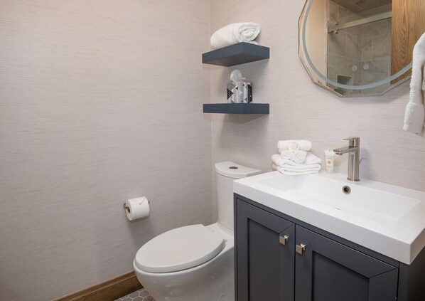 Une salle de bain moderne avec des toilettes blanches, un meuble-lavabo avec un miroir et un espace douche.