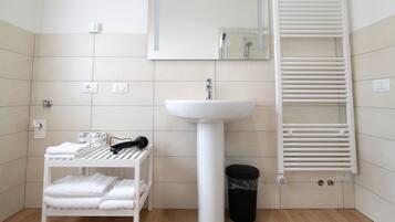 Ein Badezimmer mit einem weißen Waschbecken auf Säule, einem Handtuchhalter und einem weißen Regal mit Handtüchern.