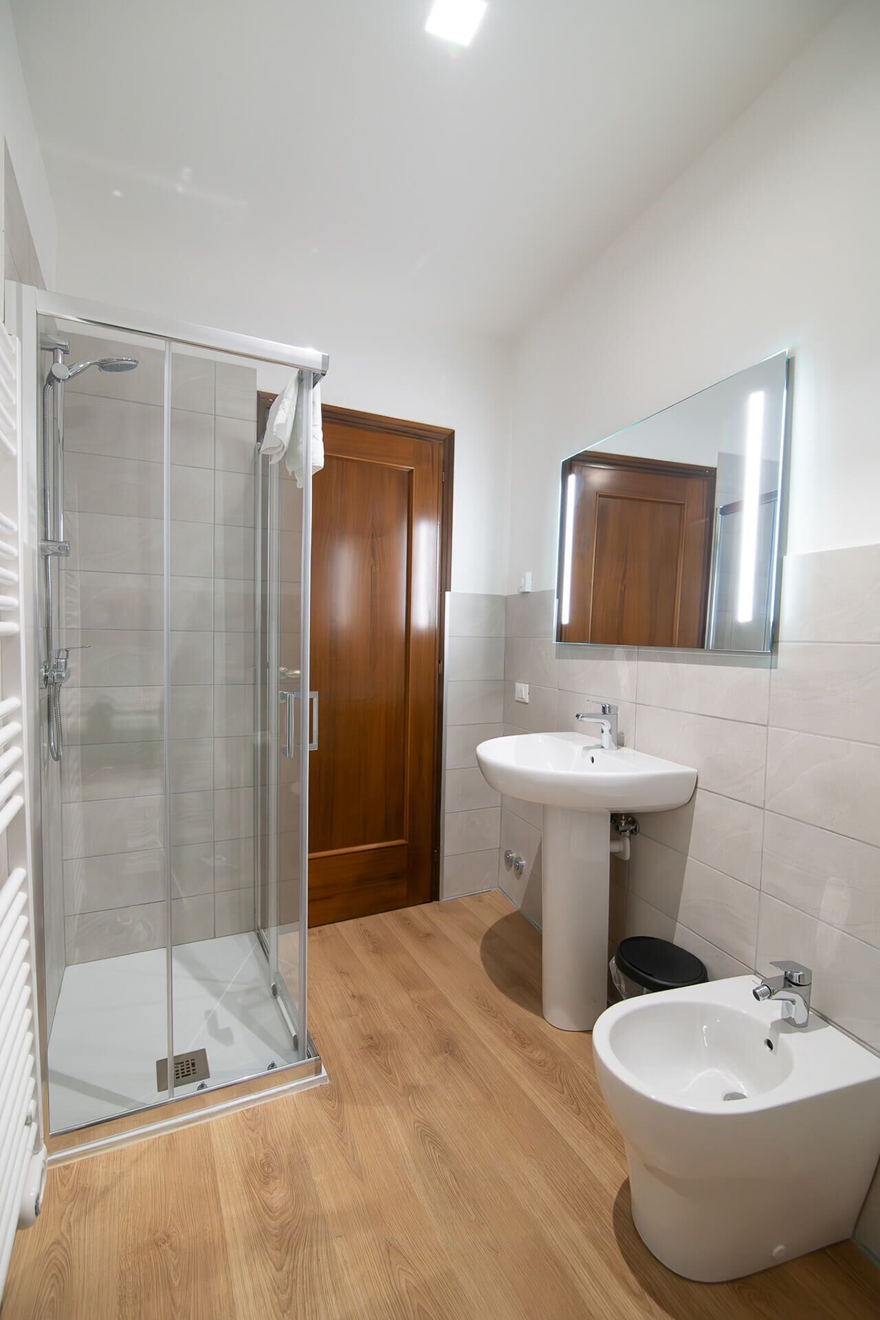 Un baño moderno con cabina de ducha de vidrio, puerta de madera, lavamanos blanco y una bañera grande.