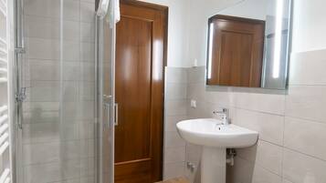 Un baño moderno con cabina de ducha de vidrio, puerta de madera, lavamanos blanco y una bañera grande.