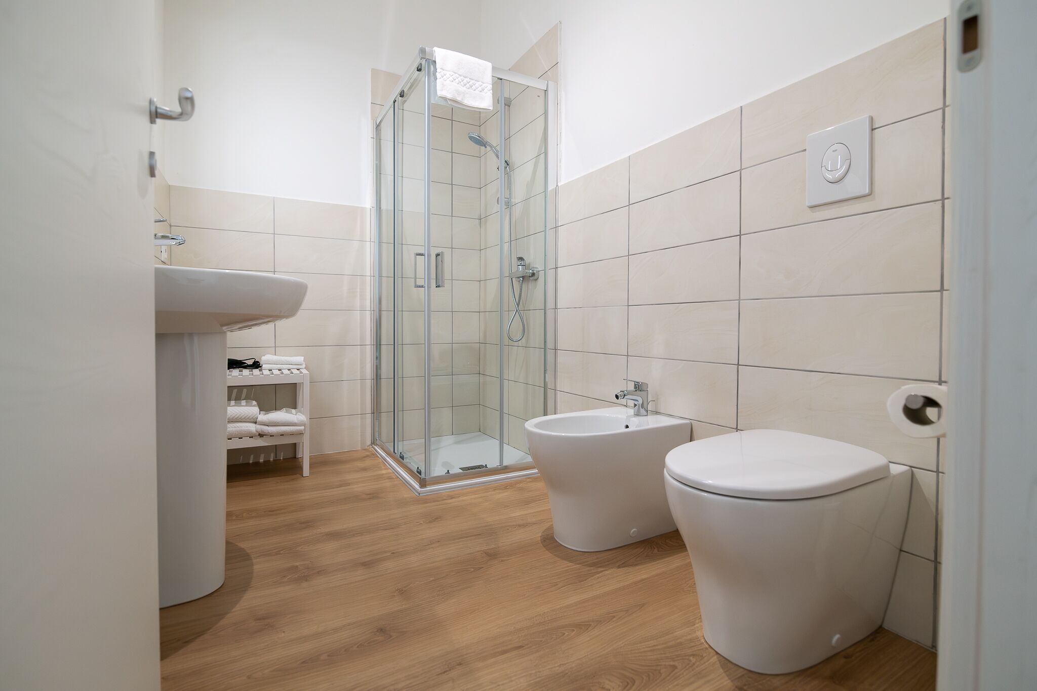 A modern bathroom with a glass shower enclosure, a pedestal sink, a bidet, and a toilet.
