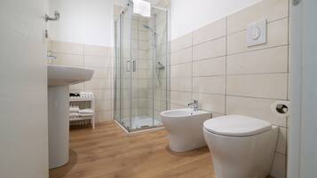 A modern bathroom with a glass shower enclosure, a pedestal sink, a bidet, and a toilet.