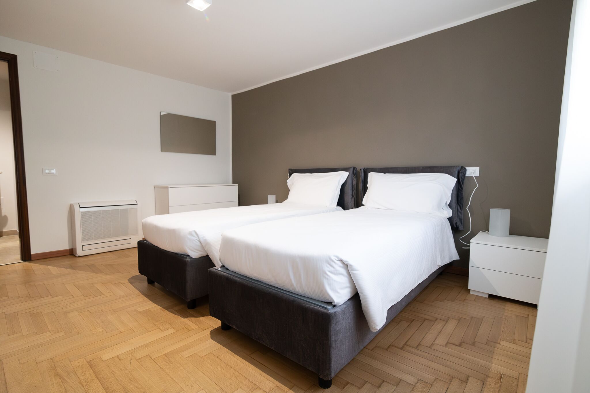 Een moderne slaapkamer met twee bedden, een witte ladekast, een nachtkastje en een spiegel aan de muur.