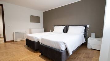 Een moderne slaapkamer met twee bedden, een witte ladekast, een nachtkastje en een spiegel aan de muur.