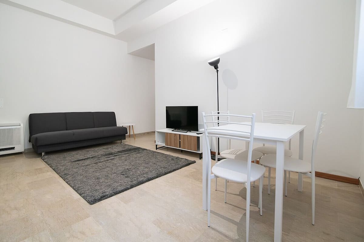 En moderne stue med sofa, fjernsyn og spisebord med stole.