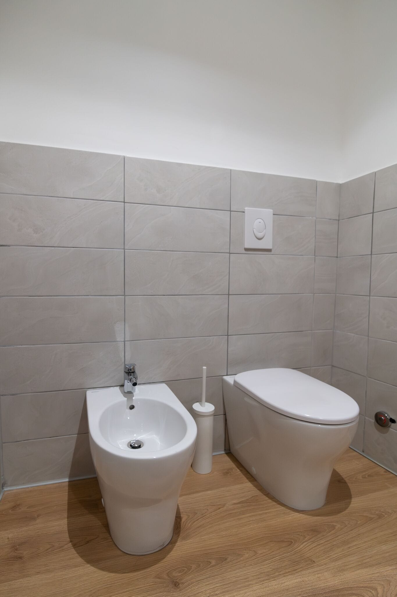 Ein Badezimmer mit einer Bidet-Funktion, Toilette und einem an der Wand montierten Spülhebel.