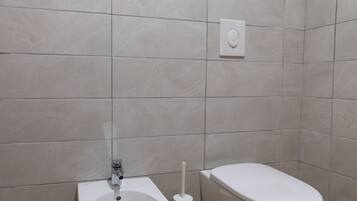 Ein Badezimmer mit einer Bidet-Funktion, Toilette und einem an der Wand montierten Spülhebel.