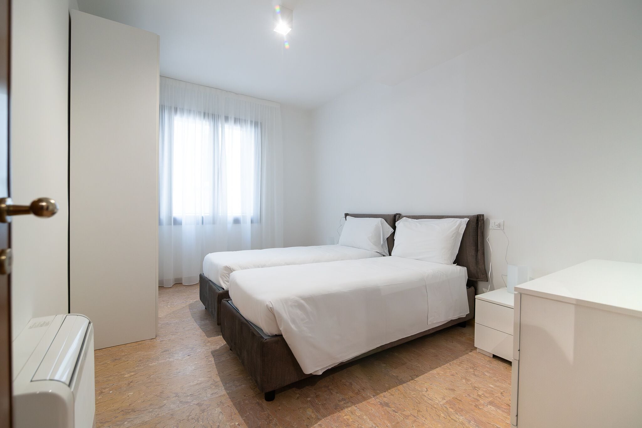 Un dormitorio con dos camas, una mesita de noche, un armario y un radiador.