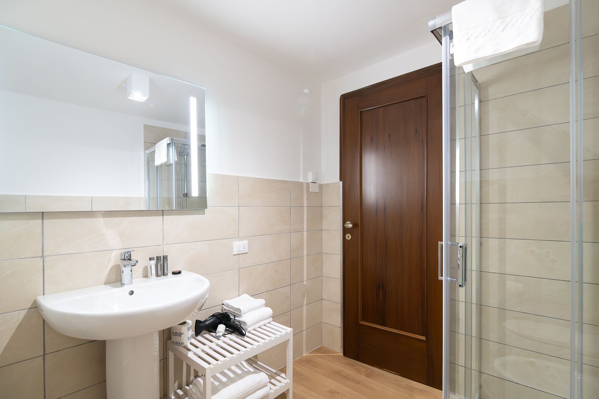 Un baño con un lavamanos blanco, un espejo, un perchero para toallas y una zona de ducha.