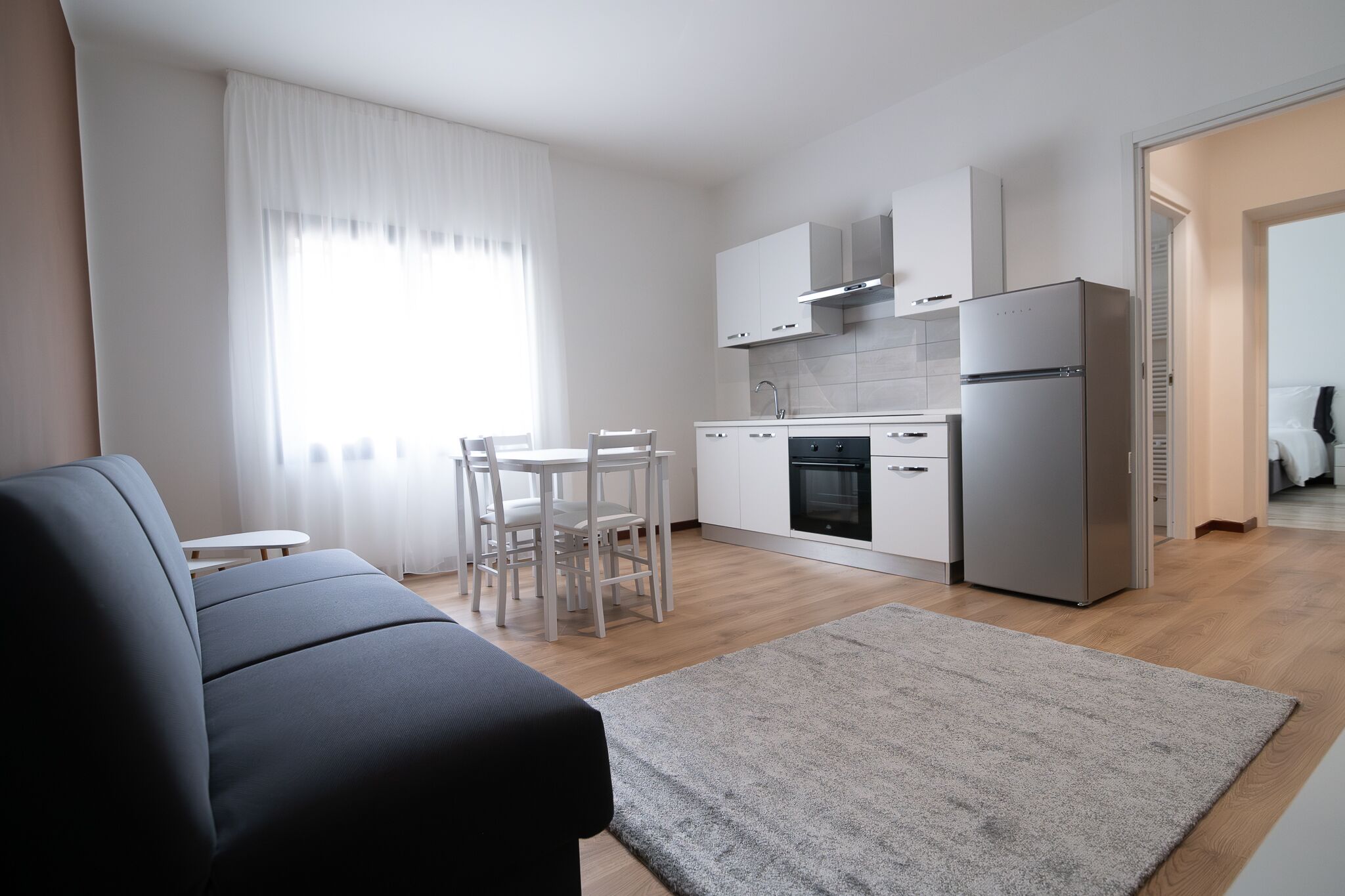 Una cocina moderna con armarios blancos, un refrigerador de acero inoxidable y una zona de comedor con mesa y sillas.