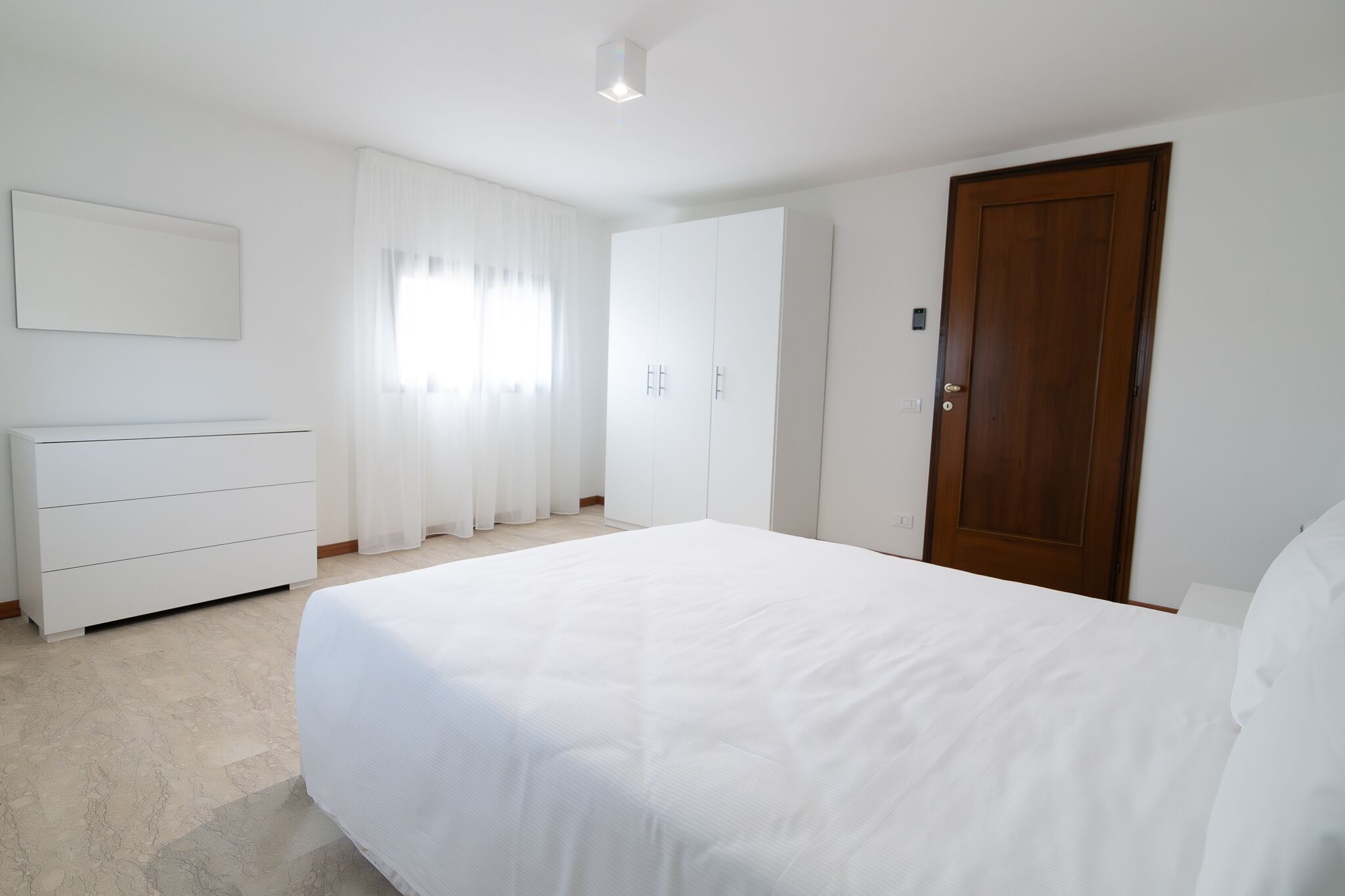 A bedroom with a bed, a dresser, a wardrobe, and a door.