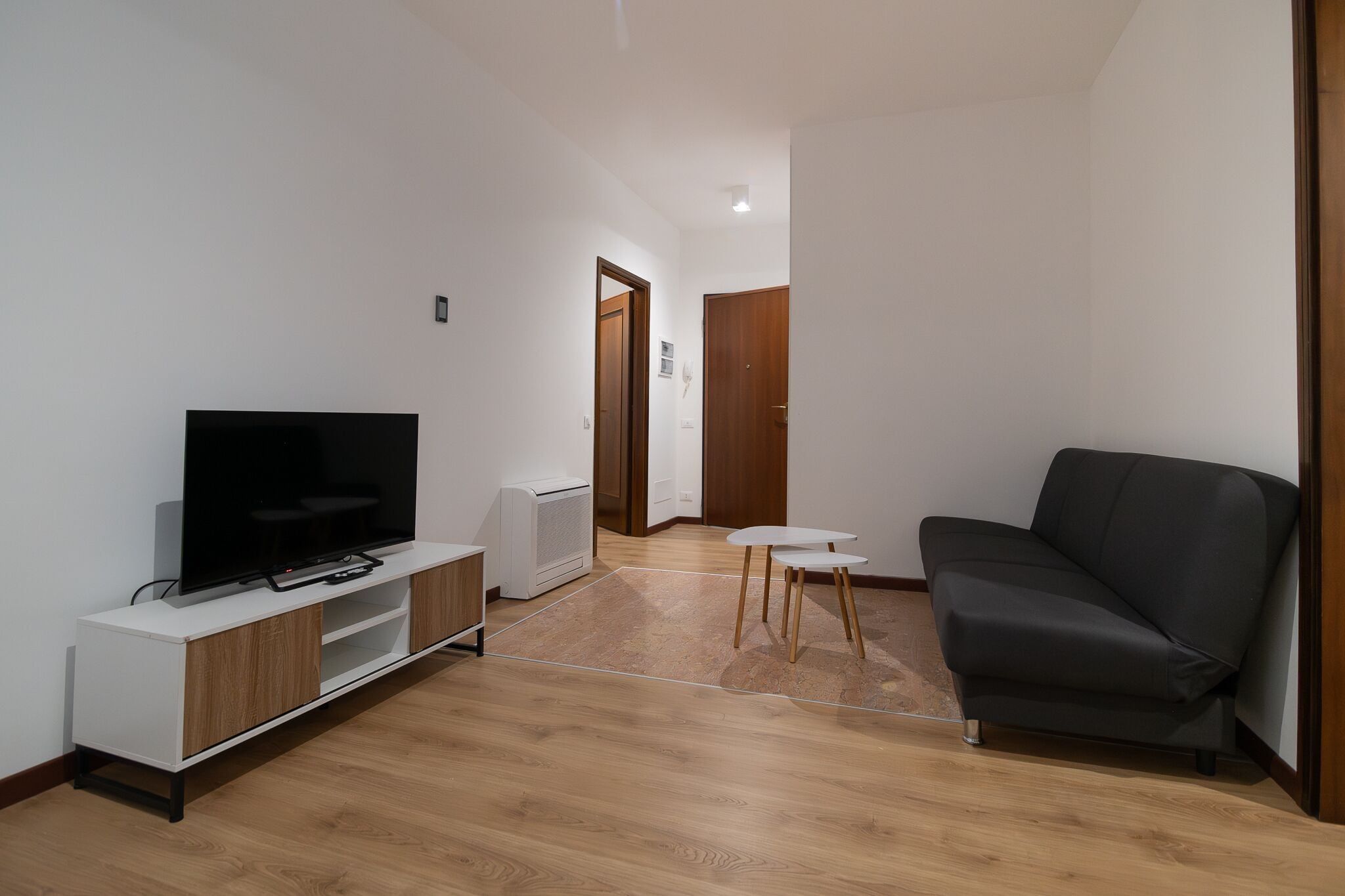A modern living room with a flat-screen TV on a white cabinet, a dark sofa, and a small white table.