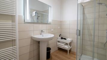 A modern bathroom with a white sink, mirror, and glass shower enclosure.