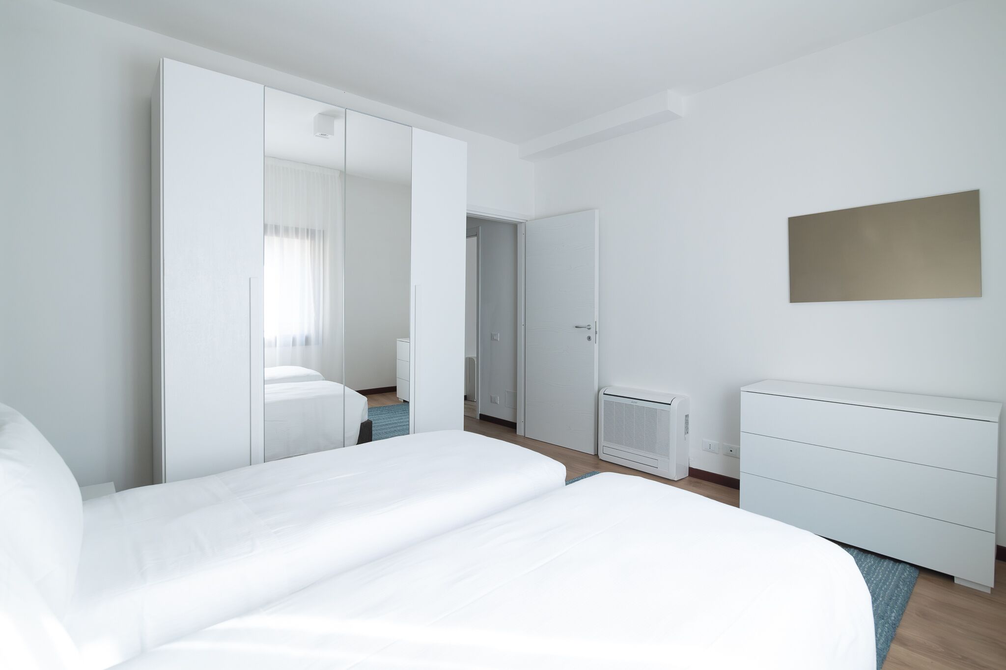 A modern hotel room with a large bed, a wardrobe, a dresser, and a radiator.