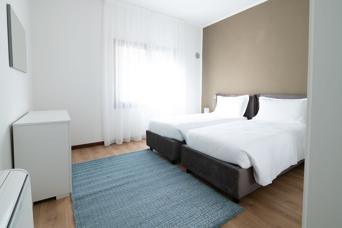 Et moderne hotelværelse med en stor seng, et lille skrivebord og et vindue med lette gardiner.