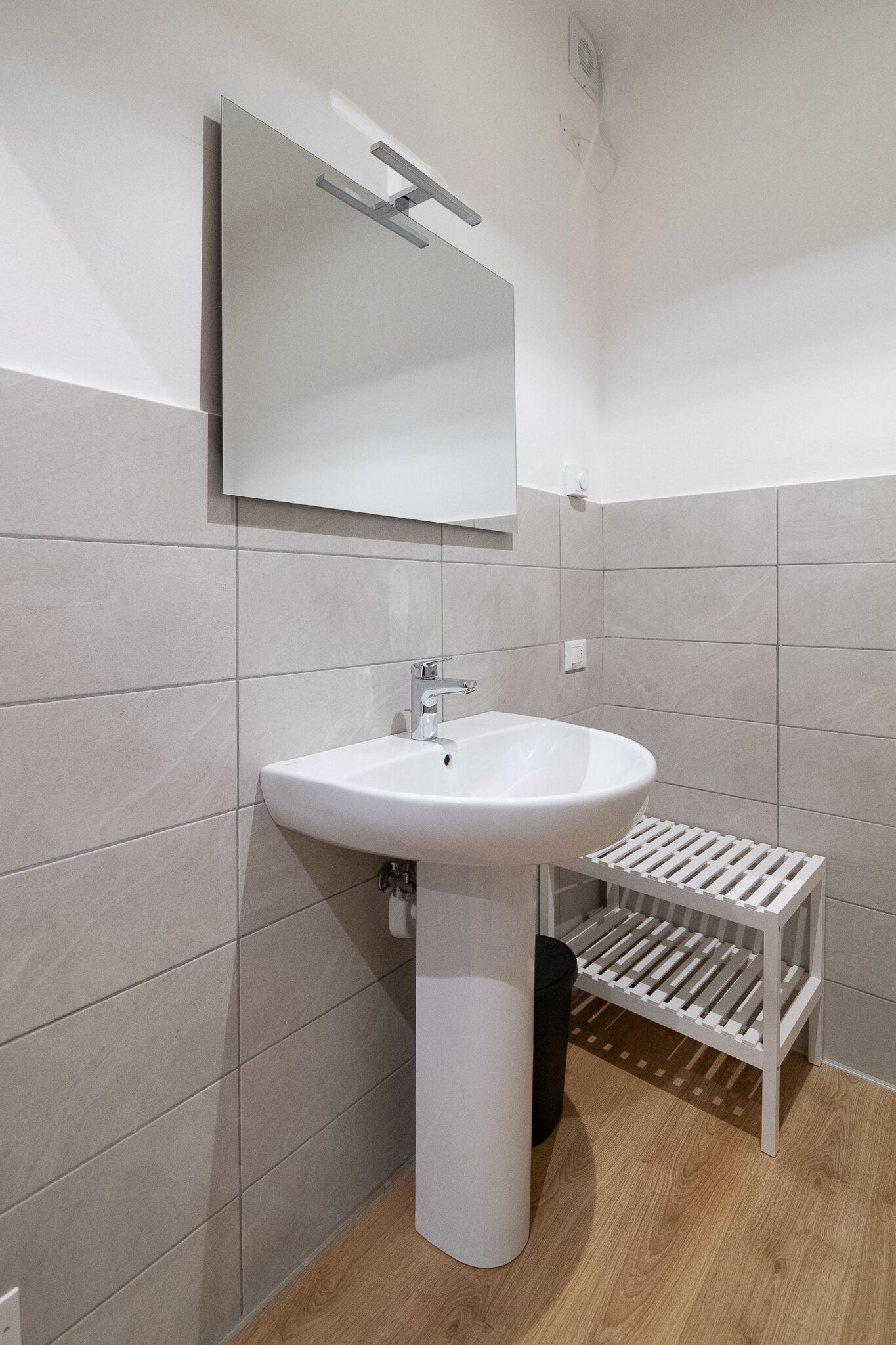 A bathroom with a white sink, a mirror, and a shelf.