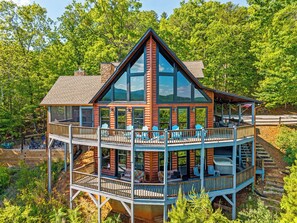 A cabin with a deck, multiple windows, and a view of the surrounding forest.