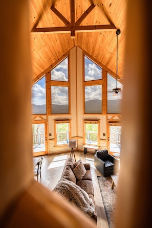 Una habitación amplia con techo alto, ventanas grandes y un rincón de descanso acogedor con sofá y sillones.