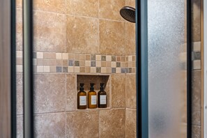 Zona de ducha con pared azulejada y repisa con tres botellas de champú, acondicionador y gel de baño.