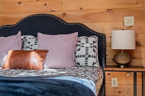A bed with patterned bedding, a nightstand with a lamp, and a wooden headboard.