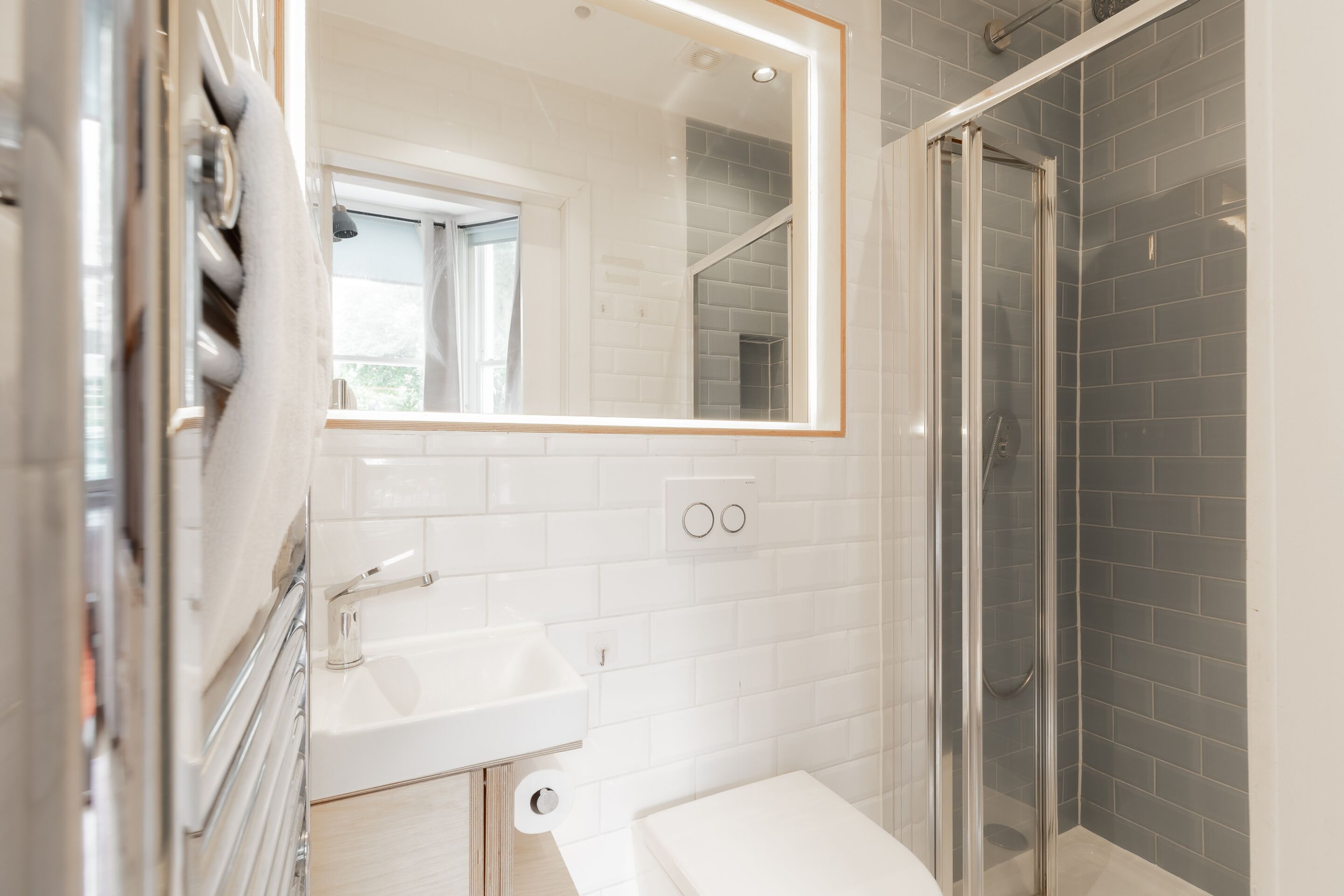 A modern bathroom with a white sink, a mirror, a glass shower enclosure, and a window.