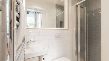 A modern bathroom with a white sink, a mirror, a glass shower enclosure, and a window.