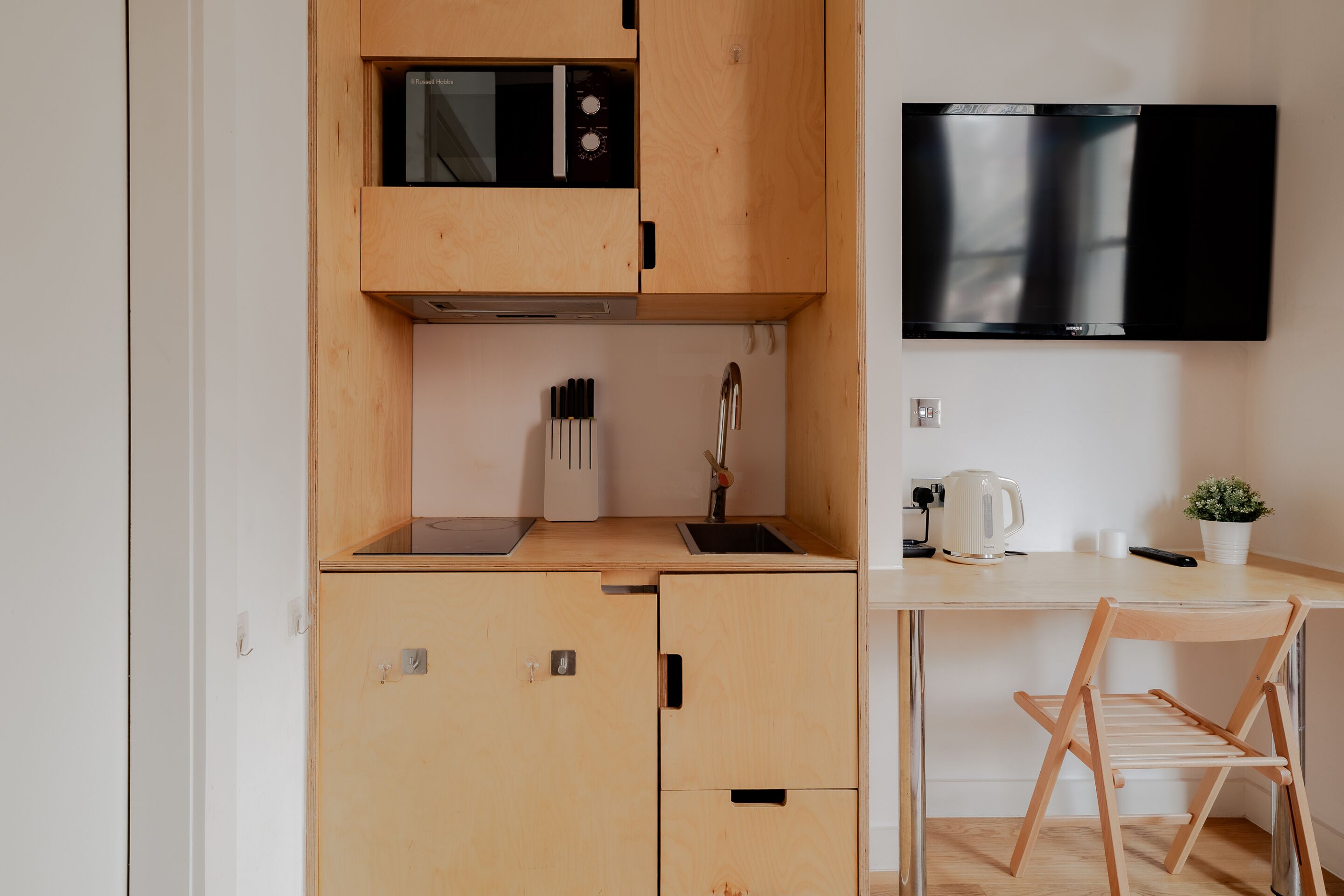 A compact kitchen with a microwave, sink, and a mounted television.