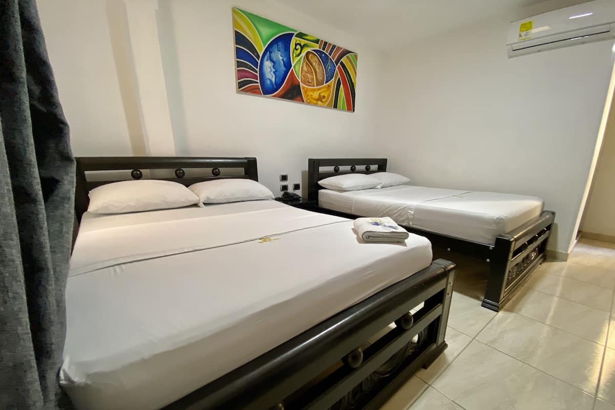 Une chambre d’hôtel avec deux lits, un tableau coloré au mur et un appareil de climatisation.