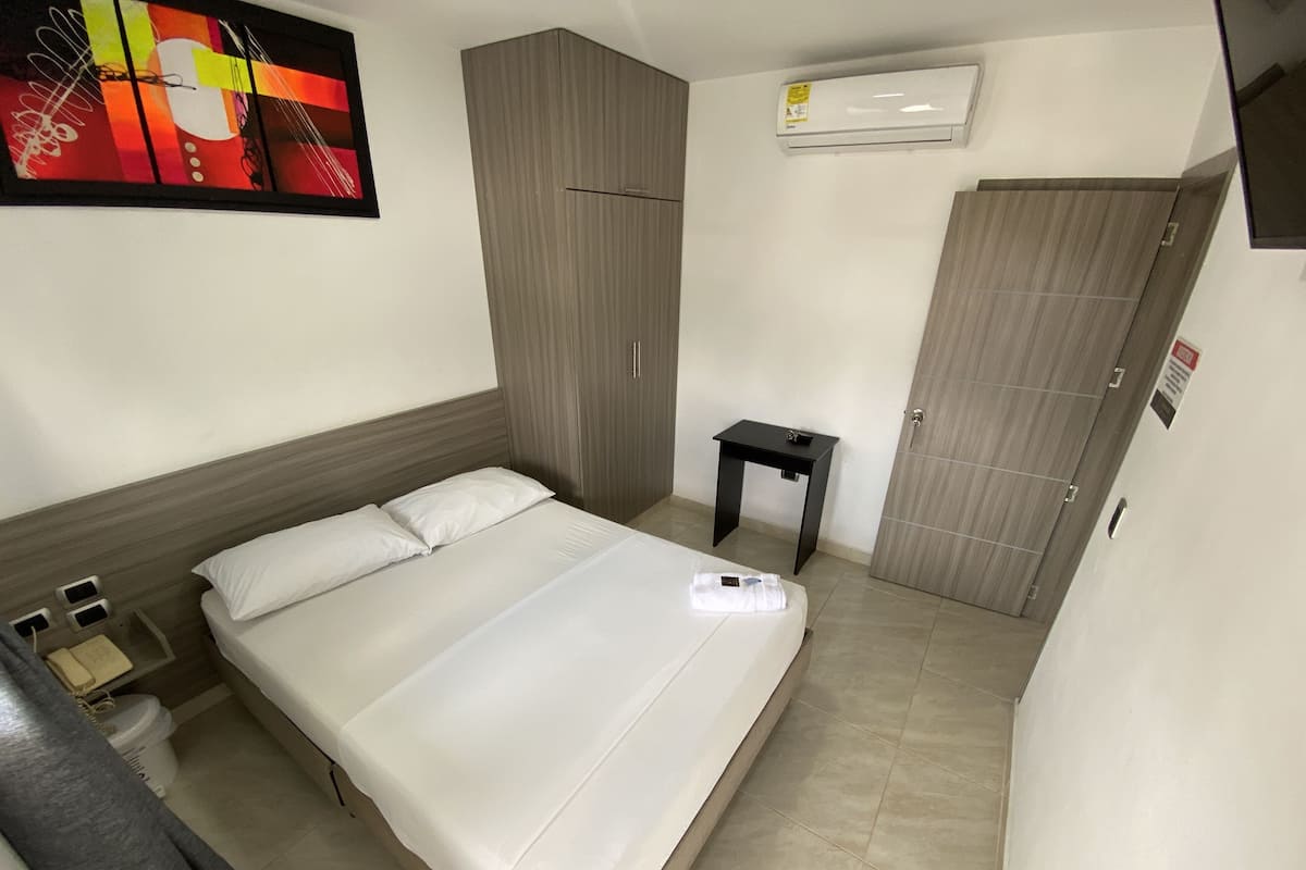 Une chambre d’hôtel comprenant un lit, une petite table de chevet, un appareil de climatisation, une armoire et une œuvre d’art murale.