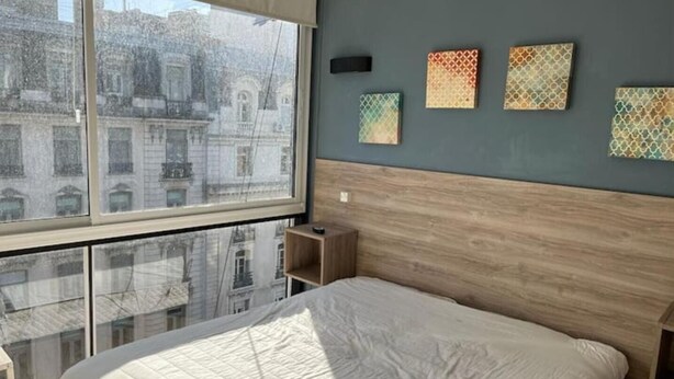 Un dormitorio con un ventanal grande, una cama y un cabecero.