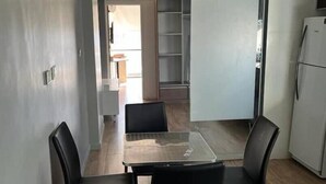 Una cocina moderna con comedor, que incluye una mesa de vidrio, sillas negras, un refrigerador blanco y una unidad de estanterías empotradas.