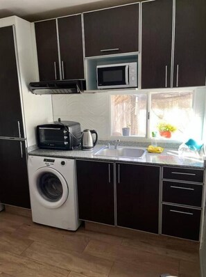 Uma cozinha compacta com armários escuros, máquina de lavar, micro-ondas e pia.