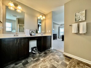 Un baño moderno con tocador de madera oscura, un espejo grande y piso de baldosas.
