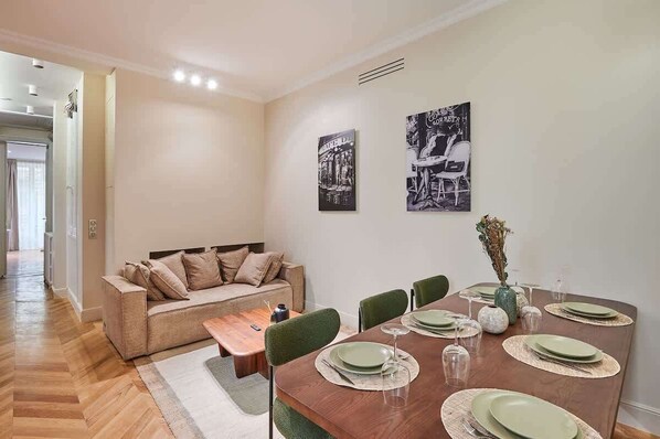 A dining area with a wooden table set for four, a sofa, and two wall-mounted black-and-white photographs. - Sublime apartment in the center of Paris (Paris)