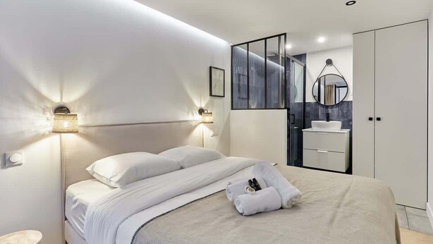 A modern hotel room with a large bed, bedside lamps, a bathroom with a mirror, and a wardrobe. - Superb apartment Arc de Triomphe (Paris)