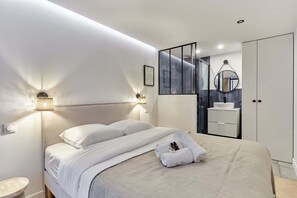 Una habitación de hotel moderna con una cama grande, lámparas de noche, un baño con espejo y un armario.