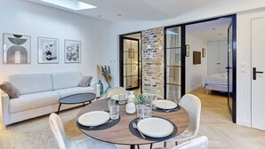 A modern living room with a dining area, a sofa, a coffee table, and a dining table set for four. There are framed pictures on the wall, a brick accent wall, and a sliding glass door leading to another room. - Superb apartment Arc de Triomphe (Paris)