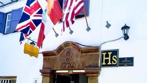 A building with a white facade, a stone entrance, and flags including the UK, US, and Spain. - Hostal Cusco Internacional (Cusco)