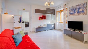 A modern living room with a red sofa, a TV, and a kitchen in the background. - Casa dei Nonni (Arco)