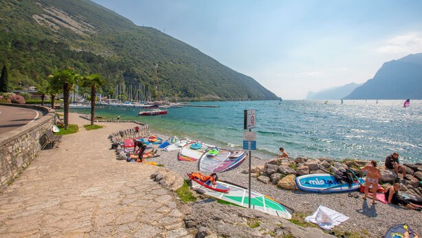 A coastal area with a stone pathway leading to a beach with boats and a mountainous backdrop. - Casa dei Nonni (Arco)