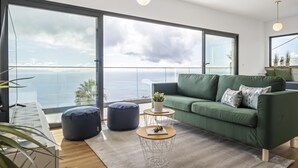 A modern living room with a green sofa, round coffee table, and a view of the ocean.