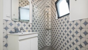 A modern bathroom with a geometric tile pattern, a glass shower enclosure, and a window providing natural light.