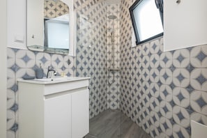 A modern bathroom with a geometric tile pattern, a glass shower enclosure, and a window providing natural light.