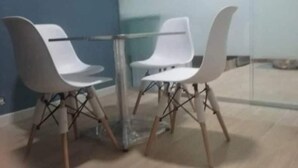 Une pièce moderne avec une table en verre entourée de chaises blanches aux pieds en bois.